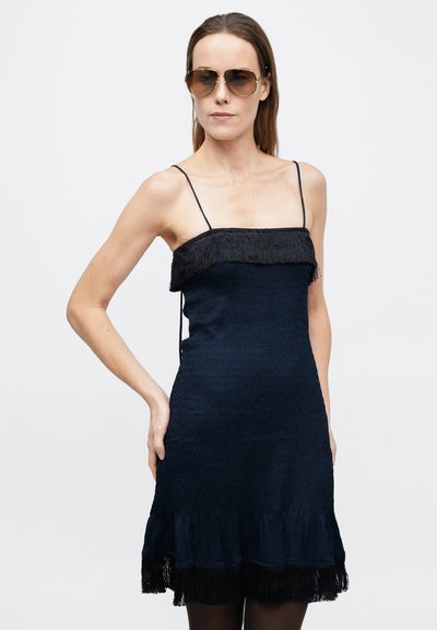 Tengerészkék, testhezálló ruha rojtos nyakkivágással és szegéllyel, texturált anyagból készült. Vékony pántokkal és bővülő sziluettel rendelkezik.