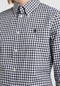 Mustavalkoinen ruudullinen paita, puuvillakangasta, nappikauluksella, valkoisilla napeilla ja pienellä brodeeratulla logolla rinnassa.