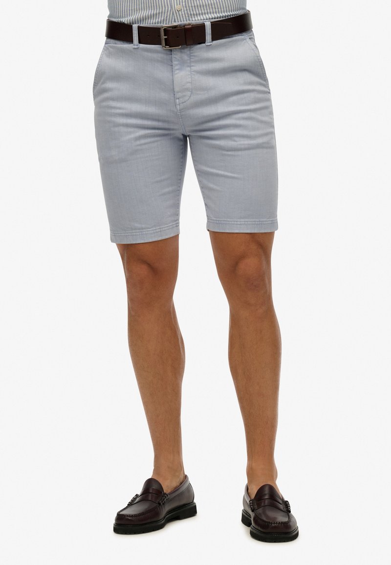 Pantaloni corti azzurri chiari con taglio dritto, realizzati in tessuto misto cotone; presentano passanti per cintura e tasche laterali; indossati con una cintura marrone scuro.