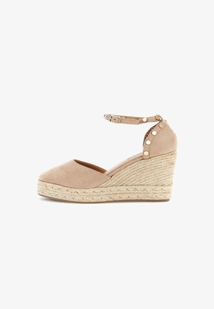 Sandale espadrille compensée en daim beige avec bride à la cheville, boucle dorée et détails cloutés sur le talon plateforme.