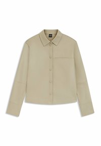 Beige Hemd mit langen Ärmeln, Knopfleiste und Kragen, mit einer einzelnen Brusttasche und minimalistischem Design, flach auf einem weißen Hintergrund ausgelegt.