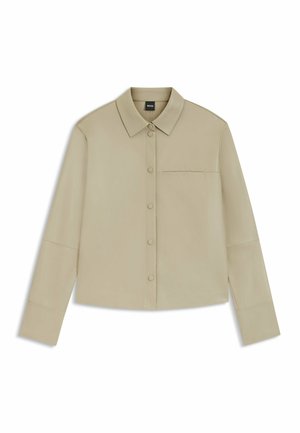 Beige overhemd met lange mouwen en knopen, voorzien van een kraag, een enkel borstzakje en een minimalistisch ontwerp, plat gelegd op een witte achtergrond.