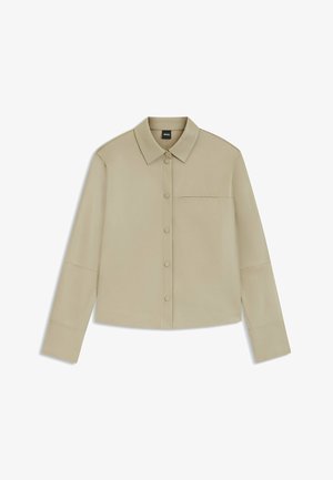 Camicia beige a maniche lunghe con bottoni, colletto, taschino singolo e design minimalista, posata piatta su uno sfondo bianco.