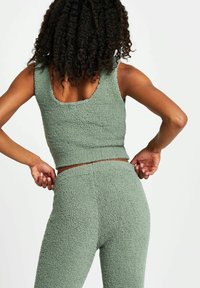 Top corto senza maniche di colore verde e pantaloni a vita alta coordinati. Il tessuto ha un aspetto morbido e peloso con un design sottile e senza cuciture.