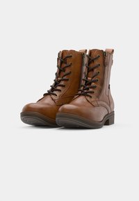 Bruna läderkängor med snörning vid vristen, sidodragkedjor och låga, staplade klackar på vit bakgrund.