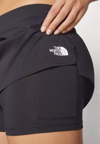 Svarta atletiska shorts med en texturerad yta, med en sidoficka och en vit logotyp av "The North Face" på midjebandet.