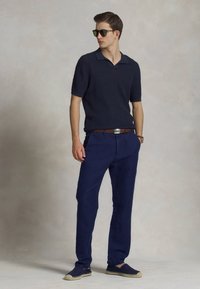 Polo shirt navy a maniche corte con una trama sottile, abbinato a pantaloni navy e espadrillas. Gli accessori includono occhiali da sole e una cintura.