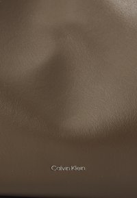 Brun skinnveske med en teksturert overflate og en sølvfarget "Calvin Klein"-logo nederst i midten.