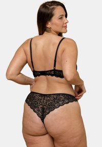 Ensemble de lingerie en dentelle noire présentant des motifs de feuilles complexes, des bretelles ajustables et des bords festonnés sur le soutien-gorge et le string. Design texturé.