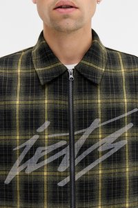 Casaco xadrez em preto e amarelo com fecho de correr, apresentando um colarinho e uma impressão gráfica proeminente na parte da frente.