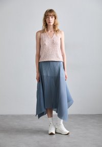Beaded blushpink ärmelloses Top mit V-Ausschnitt, kombiniert mit einem fließenden blauen plissierten Midi-Rock, getragen mit weißen Sneakers und Socken.