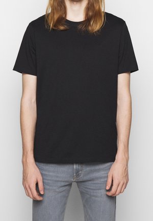 Czarna koszulka z okrągłym dekoltem, z bawełny, krótkie rękawy, subtelne logo na klatce piersiowej, w zestawie z jasnoniebieskimi przetartymi dżinsami.