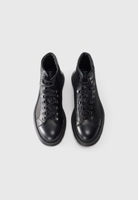 Scarpe alte nere in pelle, con occhielli in metallo, lacci spessi e un design texture sui lati e sul retro.