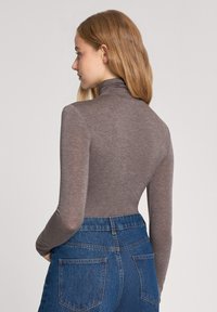 Maglione a maniche lunghe marrone con collo alto, dal design aderente, realizzato in un tessuto morbido e leggero. Abbinato a jeans in denim blu a vita alta.