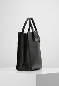 Svart läderhandväska med en strukturerad form, två överhandtag, guldfärgad hårdvara och en mjuk textur. Har dragkedjestängning och sidoficka.