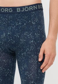 Marineblaue Boxershorts mit gemustertem Design, ausgestattet mit einem dunklen Bund, auf dem "BJÖRN BORG" in hellgrau steht. Glattes, dehnbares Material.