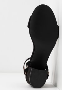 Black suede high-heeled sandal with thin straps and a textured black rubber sole. Size 37 marked on the sole.