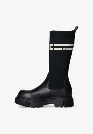 Stivale alla caviglia in pelle nera con altezze in maglia a coste nera, caratterizzato da strisce bianche e logo. Suola spessa e strutturata per una maggiore trazione.