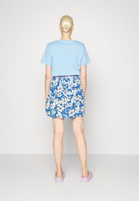 T-shirt de manga curta azul claro combinado com uma saia floral azul estampada. Calçado é de um tom roxo pastel. Vista de trás, textura suave.