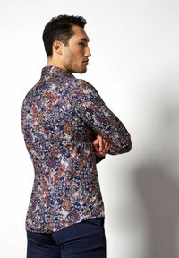 Dunkelblaues Langarmshirt mit einem mehrfarbigen Blumen- und Paisleymuster, taillierter Schnitt und abgerundetem Saum. Modell steht seitlich.