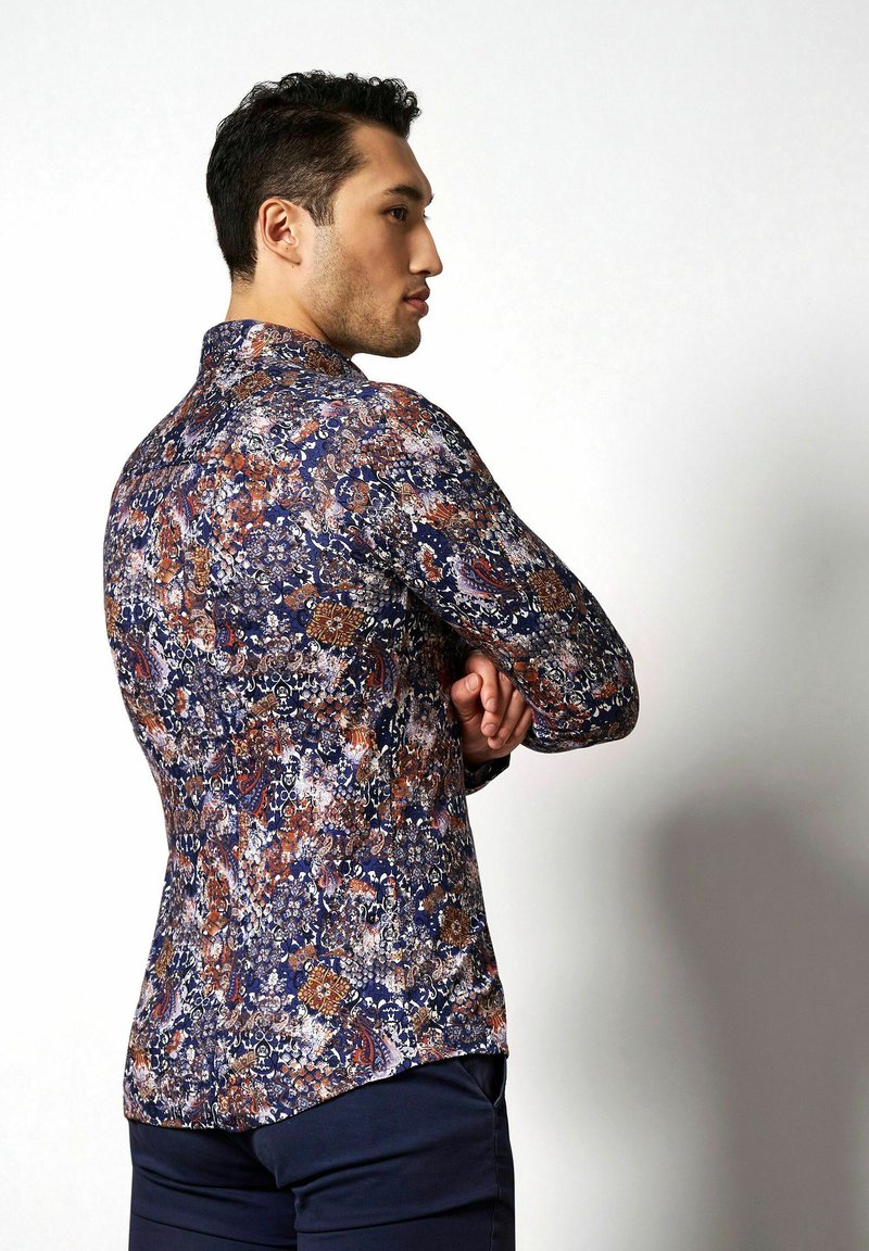 Dunkelblaues Langarmshirt mit einem mehrfarbigen Blumen- und Paisleymuster, taillierter Schnitt und abgerundetem Saum. Modell steht seitlich.
