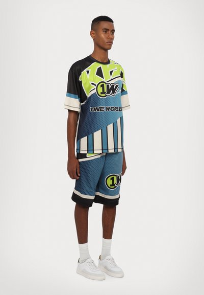 Costum sportiv grafic, format dintr-o cămașă cu mânecă scurtă, multicoloră, cu imprimeuri îndrăznețe și șorturi albastre asortate. Fabricat din material mesh respirabil.