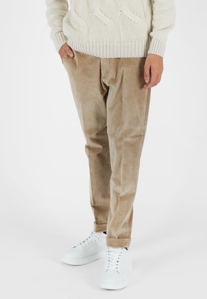 Pantaloni in corda beige con una vestibilità rilassata, caratterizzati da righe verticali e tasche laterali, abbinati a sneakers bianche.