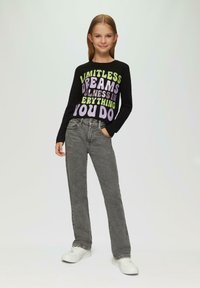Schwarz langärmliges Shirt mit buntem Text; graue gerade Jeans; weiße Sneakers. Einfaches, lässiges Outfit mit modernem Design.