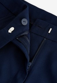 Pantaloni in tessuto blu navy con chiusura a bottoni e zip, caratterizzati da una texture liscia e dettagli metallici per la chiusura.