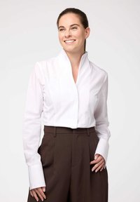 Blusa bianca con colletto, maniche lunghe e polsini larghi, abbinata a pantaloni marroni a vita alta. Tessuto liscio e design elegante.
