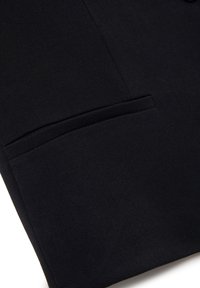Blazer nero con un tessuto liscio e dalla consistenza particolare, dotato di una singola tasca e una vestibilità strutturata. Design minimalista senza hardware visibile.