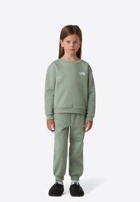 Light green sweatshirt and matching sweatpants in soft fabric, featuring a small logo on the chest and hip. Worn with black slip-on shoes.