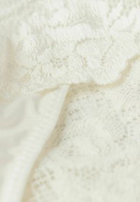 Vitt spetstyg med intrikata blommönster, lager på ett jämnt, solitt vitt material, med texturerade kanter och fina detaljer.