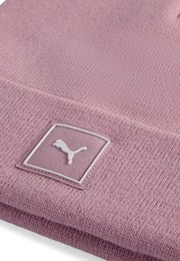 Gorro de punto rosa con un patrón texturizado y un parche rectangular blanco que presenta un logotipo. El material parece suave y flexible.
