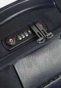 Valigia blu navy con meccanismo di chiusura a zip con combinazione a quattro cifre, doppie zip e una superficie in pelle liscia su un lato.