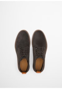Donkergrijze suède schoenen met een ronde neus, vetersluiting en bruine leren accenten bij de hak en de rand van de zool.