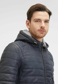 Giubbotto di pelle trapuntato blu navy con cappuccio grigio. Presenta una chiusura con zip, spalle a coste e una texture liscia per calore e stile.