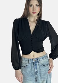 Schwarzes, tailliertes Oberteil mit V-Ausschnitt, mit Puffärmeln und Knopfdetails an der Vorderseite, kombiniert mit hochgeschnittenen, hellblauen Jeans.