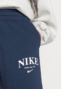 Marinblå Nike-mjukisbyxor med elastisk midja. Har vit tryckt logotyp och texten "Athletic dept. 1972" på låret. Mjuk tygkänsla.