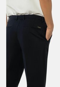 Hosen in Marineblau aus glattem Stoff, mit Gesäßtaschen, Gürtelschlaufen und einem kleinen metallischen Markenakzent am Bund.