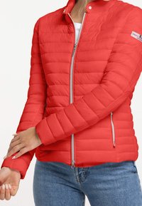Chaqueta inflable roja con cremallera frontal y cuello alzado, que presenta líneas de acolchado horizontal y bolsillos laterales con cremallera. Tejido suave y liviano.