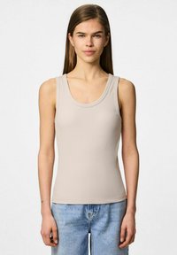 Beżowy prążkowany top na ramiączkach z okrągłym dekoltem i szerokimi ramiączkami, w zestawie z jasnoniebieskimi dżinsami. Gładki materiał z dopasowanym krojem.