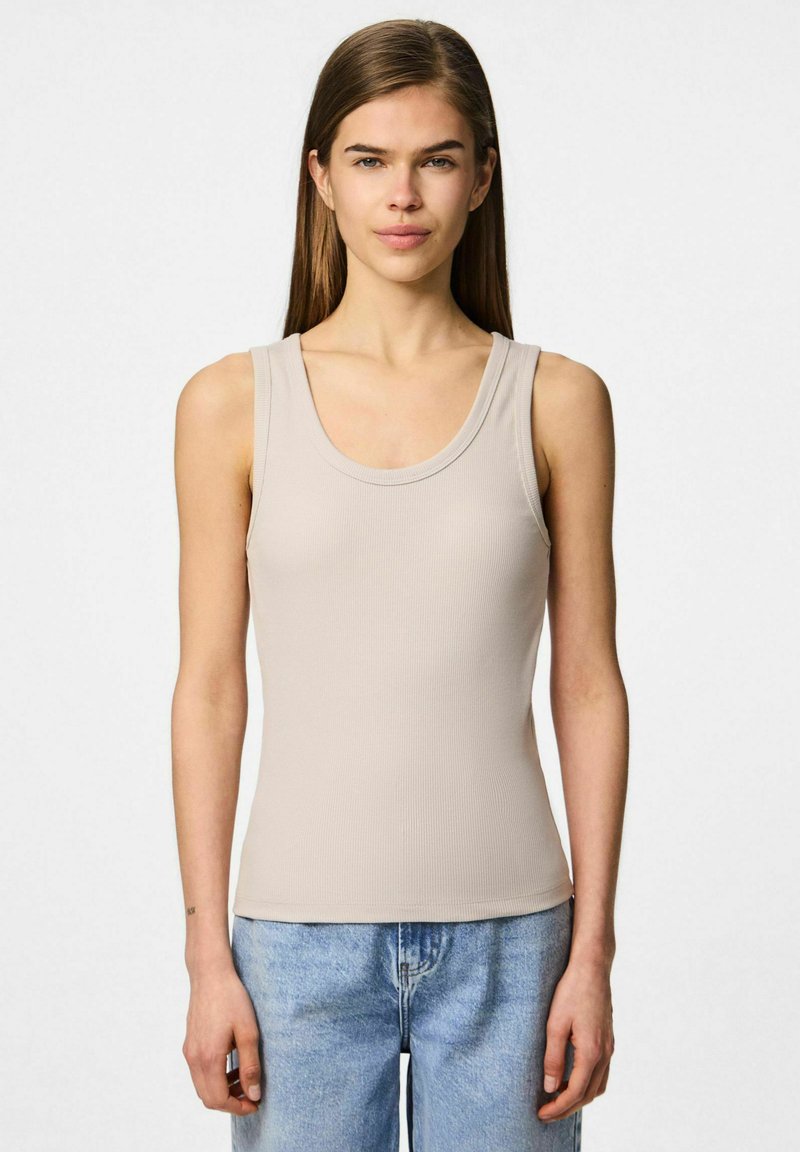 Beżowy prążkowany top na ramiączkach z okrągłym dekoltem i szerokimi ramiączkami, w zestawie z jasnoniebieskimi dżinsami. Gładki materiał z dopasowanym krojem.