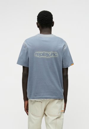 Heledad sin varrukatega helesinine T-särk, millel on ümar kaelus, tagaküljel tuhm logo ja varrukal aksenttaga.