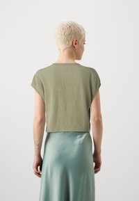 Top accorciato a maniche corte in tessuto verde oliva chiaro con una texture liscia; abbinato a una gonna in satin verde menta elegante.