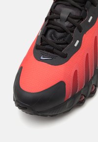 Chaussure de sport rouge et noire avec un dessus texturé, des détails en mesh et une semelle en caoutchouc comportant des coussins d'air. Logo Nike présent.