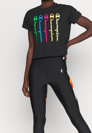 Zwarte cropped Champion t-shirt met meerkleurige verticale logo's, gecombineerd met zwarte leggings met oranje en witte zijstrepen.