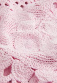 Blød lyserød strikket tæppe med hævede cirkulære og blomsteragtige mønstre, der viser tekstureret garn og detaljeret syning.