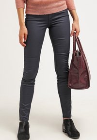 Pantaloni grigi, aderenti, con una texture liscia e raffinata. Indossati con un maglione di lana rosa e una borsa bordeaux dalla texture particolare. Stivali neri alla caviglia completano il look.