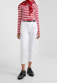 Camicetta a maniche lunghe a righe rosse e bianche, pantaloni bianchi cropped, scarpe con tacco nero con bordi bianchi e una sciarpa rossa a motivo attorno al collo.